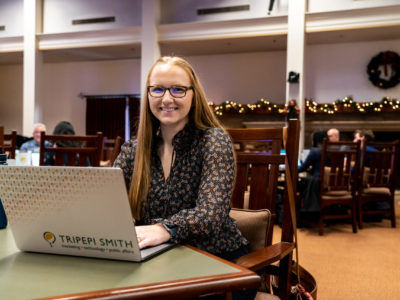 Sara Madsen, smiling, working on her laptop.